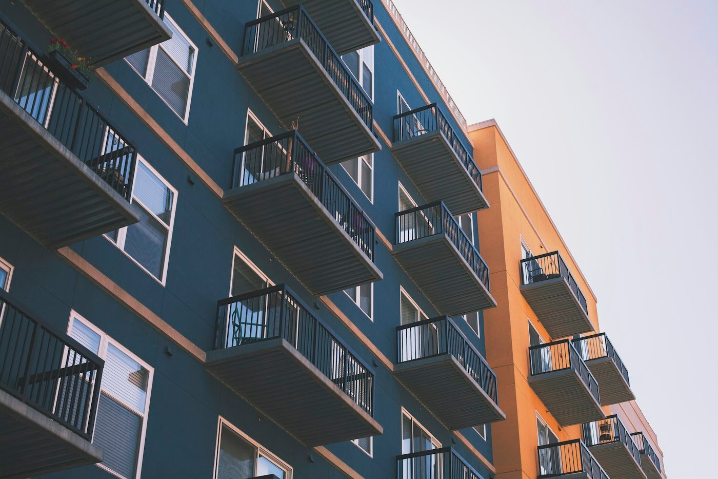 Blue and orange apartment facade with stacked metal balconies and white window frames