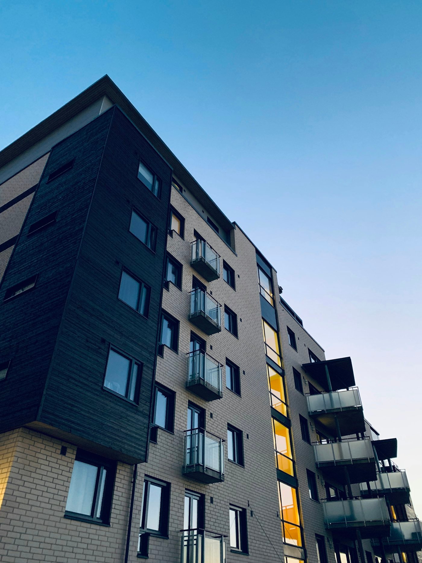 A brick apartment block with glass balconies and a dark timber section on the corner